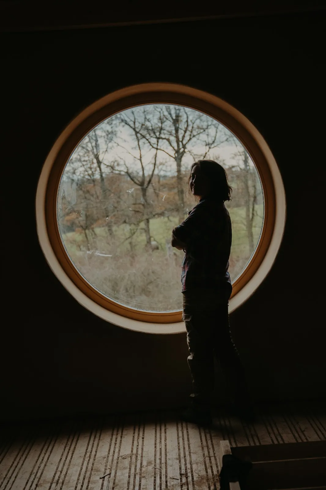 Denisa Divoká standing by a round window on site, landscape behind